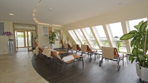 A sunlit room with multiple lounge chairs, large windows, and potted plants. - Hotel Adlerbräu (Gunzenhausen)