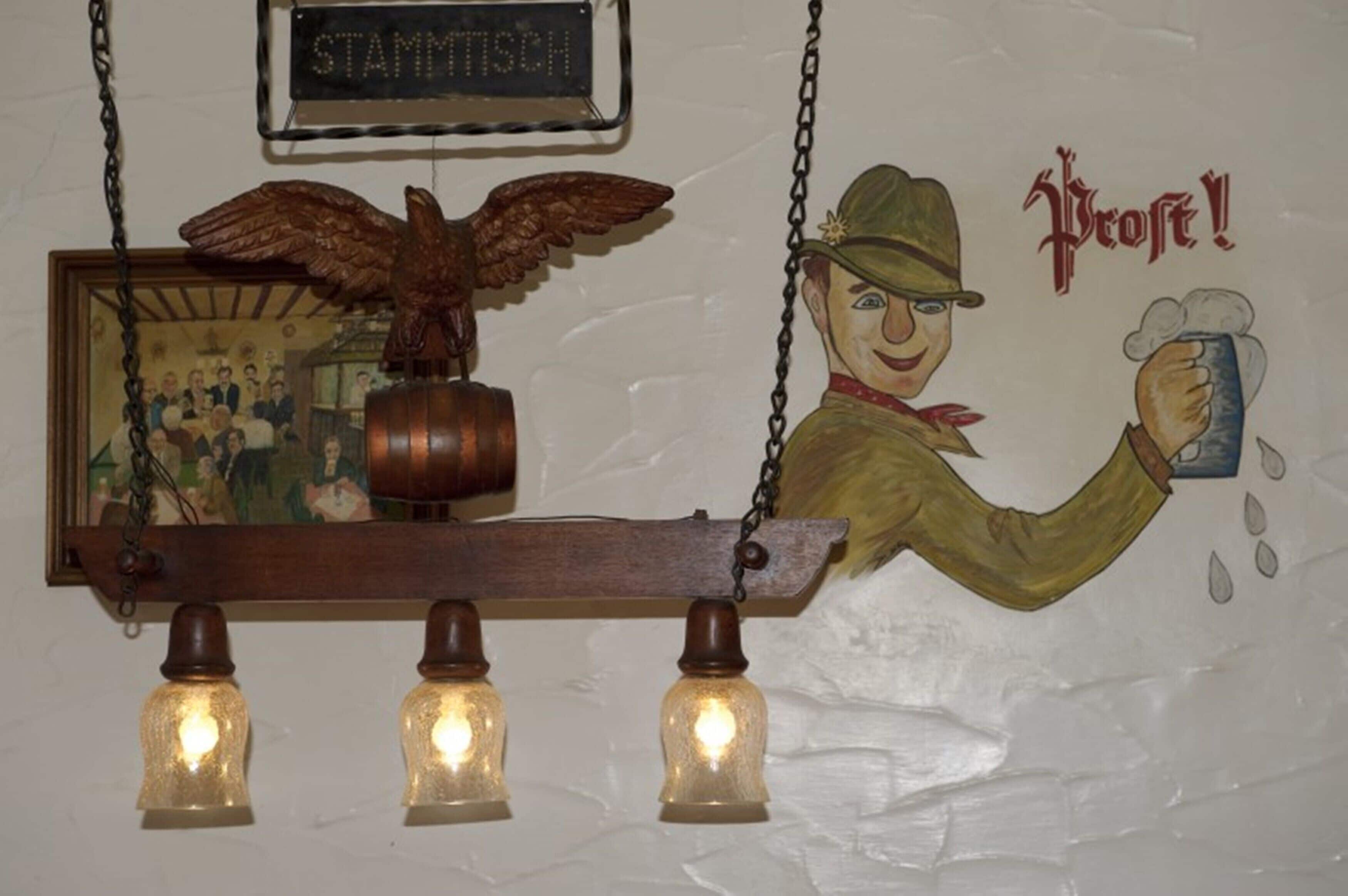 Decoración de pared con un letrero de madera que dice "STAMMSTICH", un barril de madera y una figura sosteniendo un vaso de cerveza con la palabra "Profe".