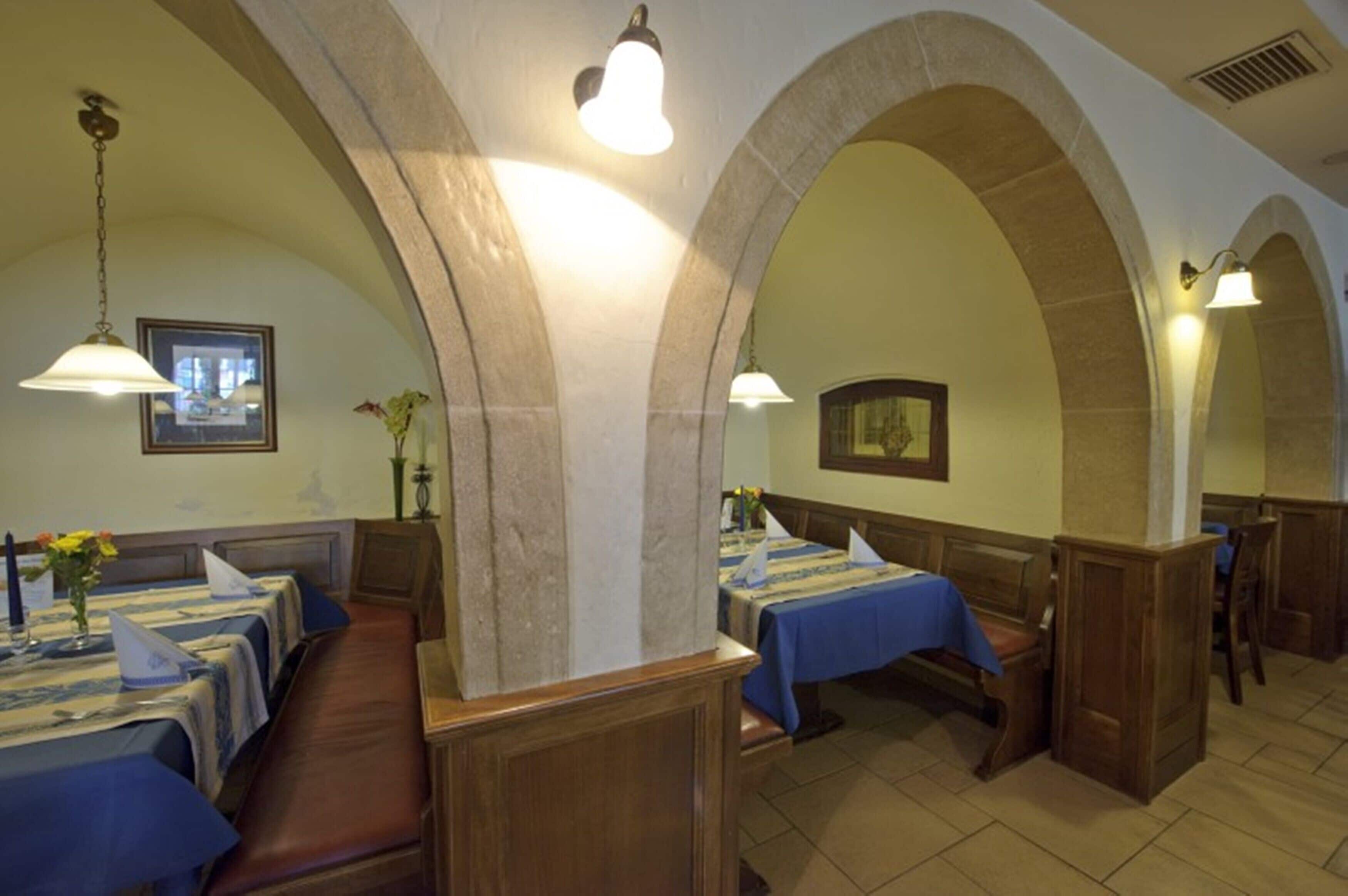 A restaurant with high arched ceilings, wooden benches, and tables covered with blue tablecloths.