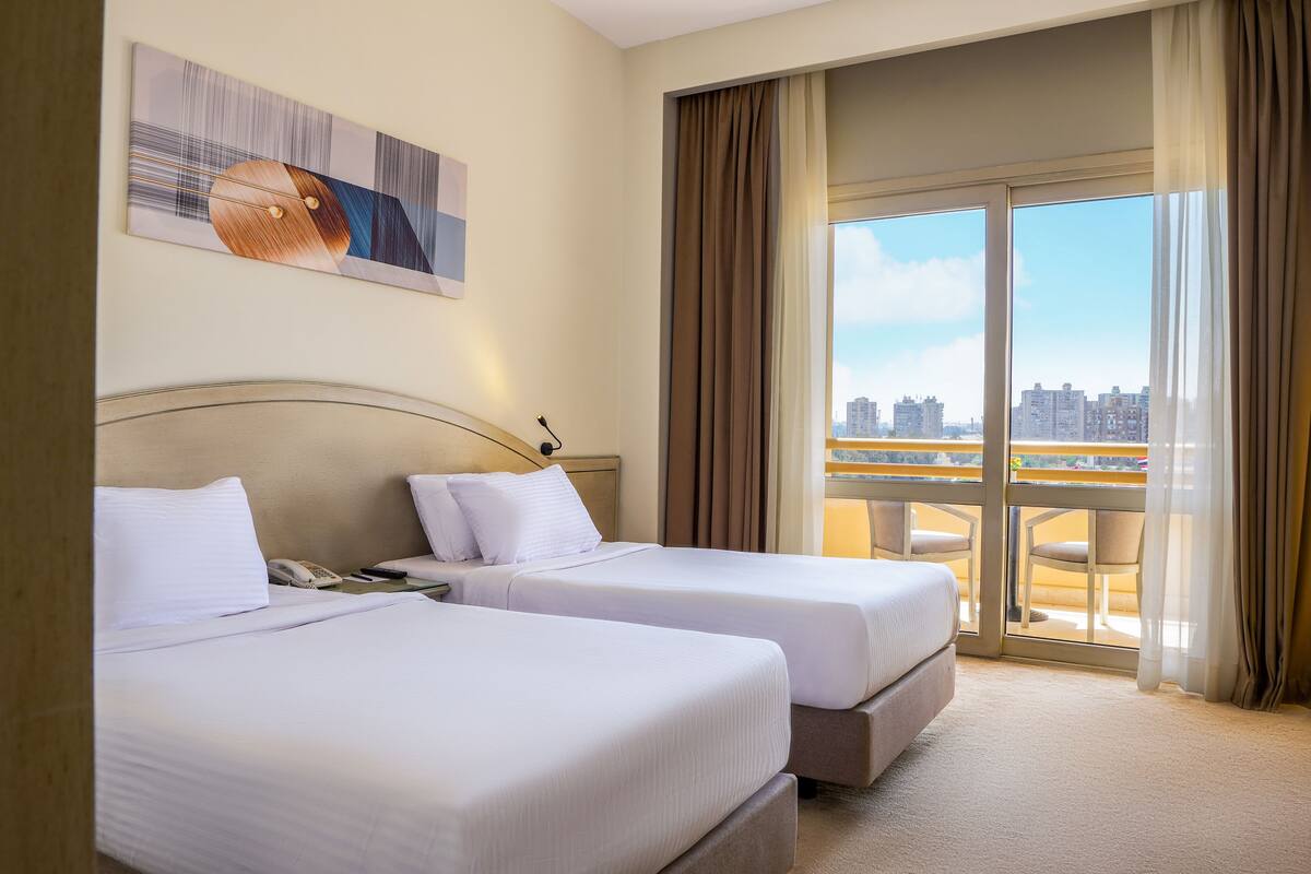 A hotel room with two beds, a city view, and a balcony with chairs.