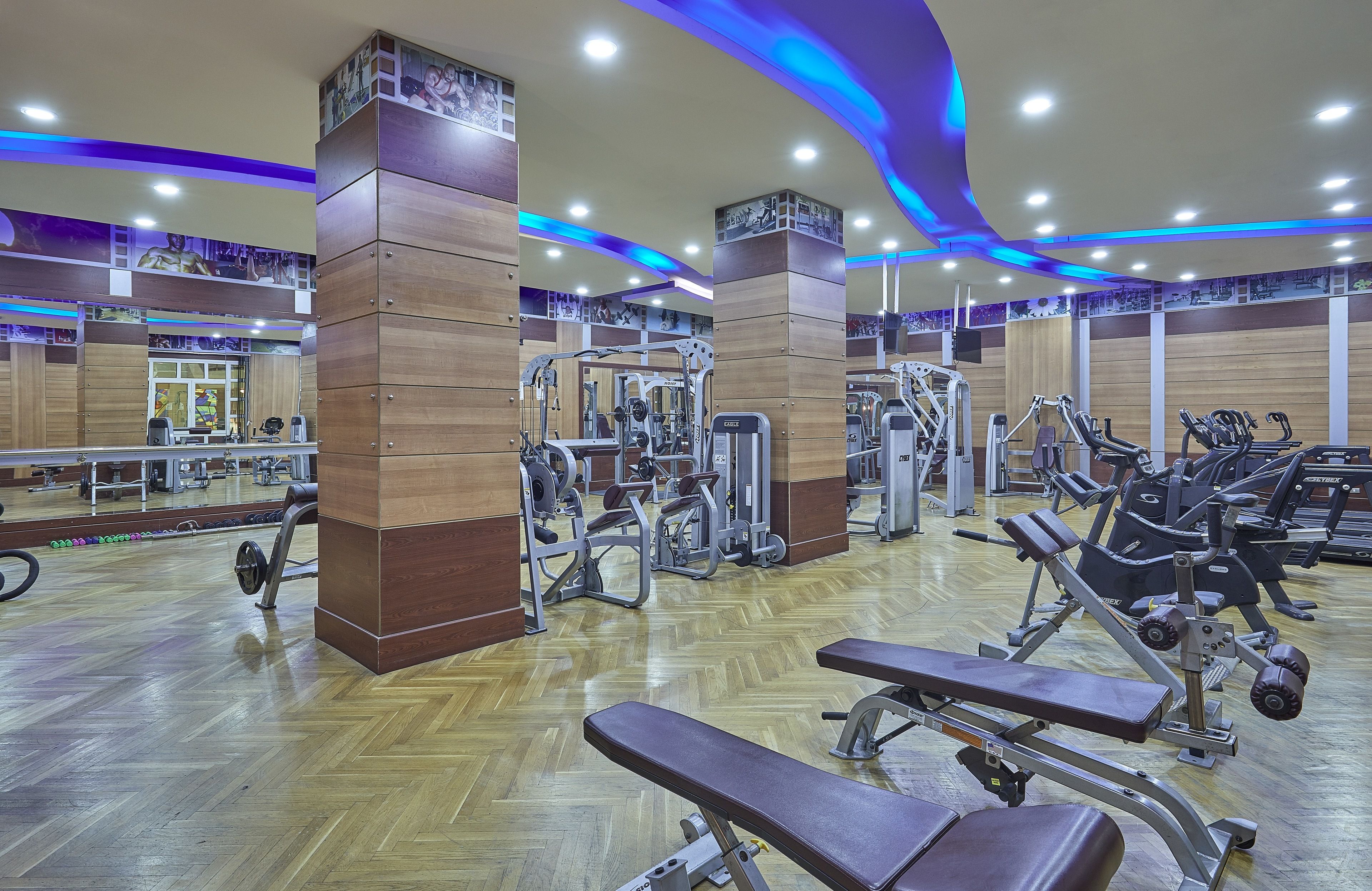 A gym with various exercise equipment, wooden floors, and mirrored walls.