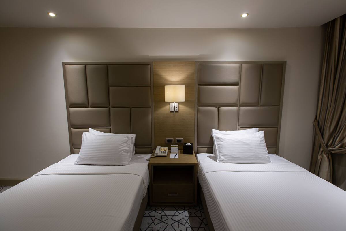 A hotel room with two beds, a nightstand with a lamp, a phone, and a small table.