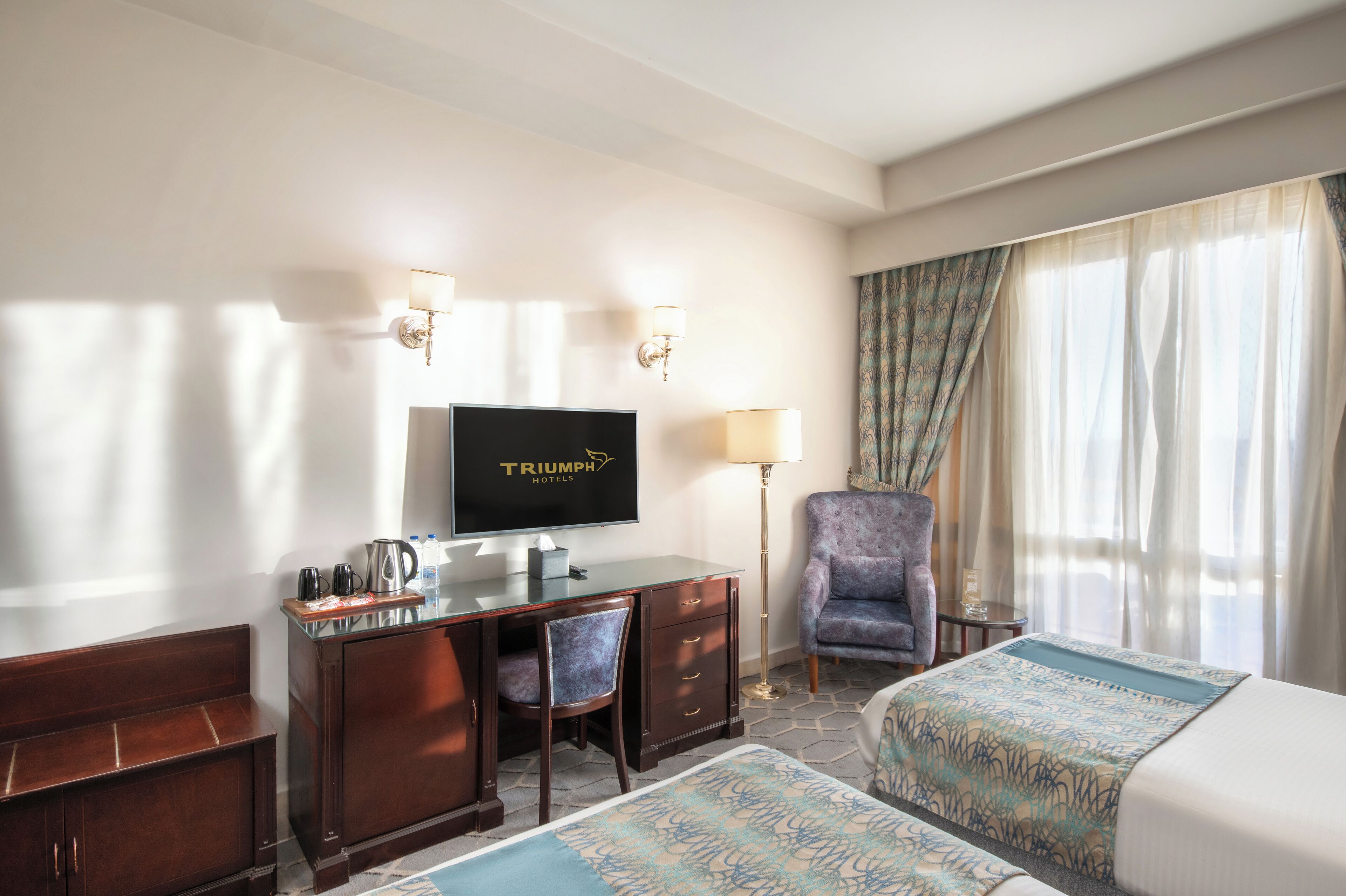 Habitació d'hotel amb un llit, un escriptori, televisió de pantalla plana, una cadira, una làmpada i una finestra amb cortines.