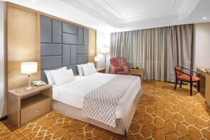 A hotel room with a large bed, a desk, a chair, and a nightstand with a lamp. - Triumph Plaza Hotel (Cairo)
