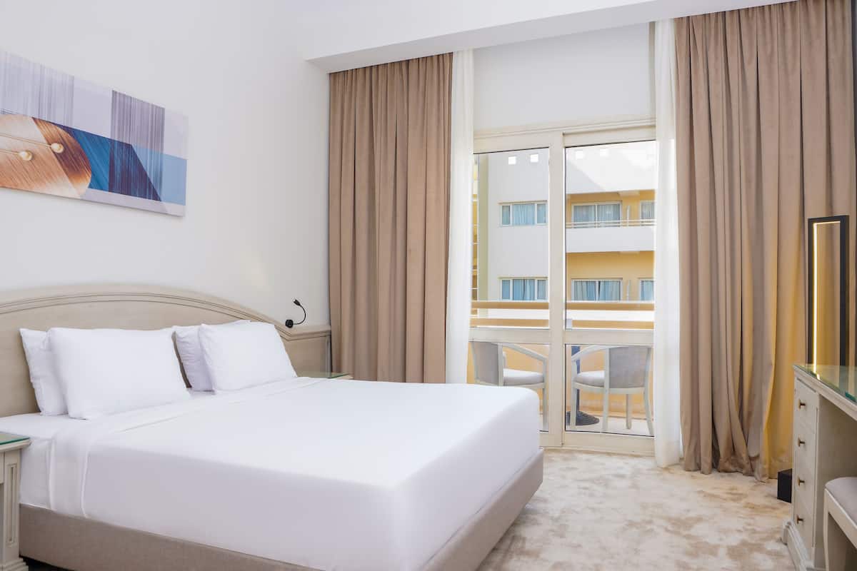 A hotel room with a bed, a nightstand, a TV, and a balcony with curtains.