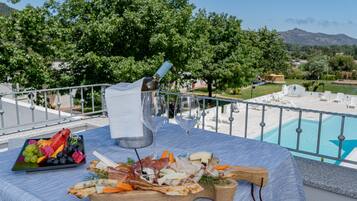 A table with a charcuterie board, wine glasses, and a view of a pool and mountains.
