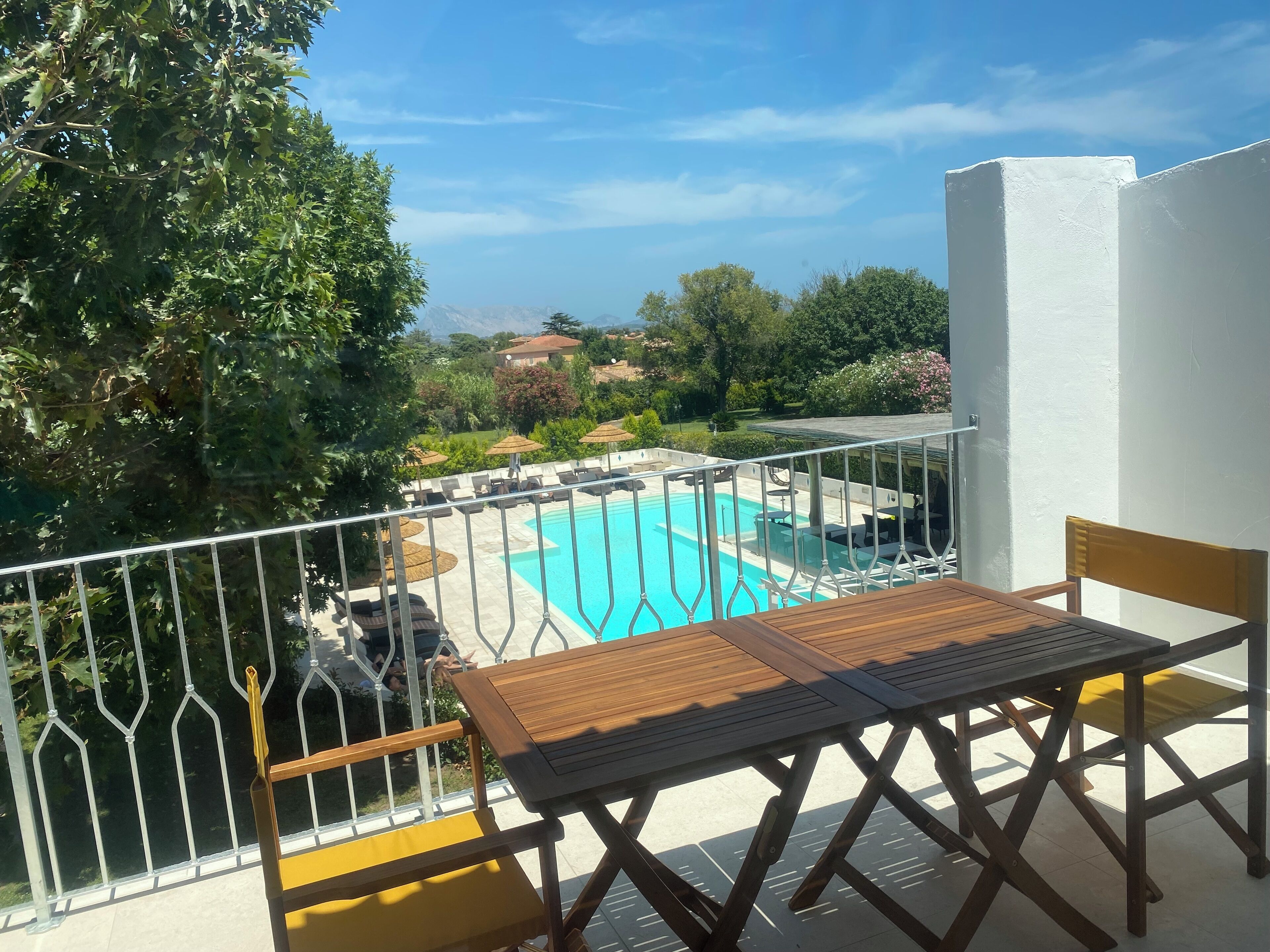 Ein Balkon mit Blick auf einen Swimmingpool, Sitzmöglichkeiten im Freien und umliegendes Grün.