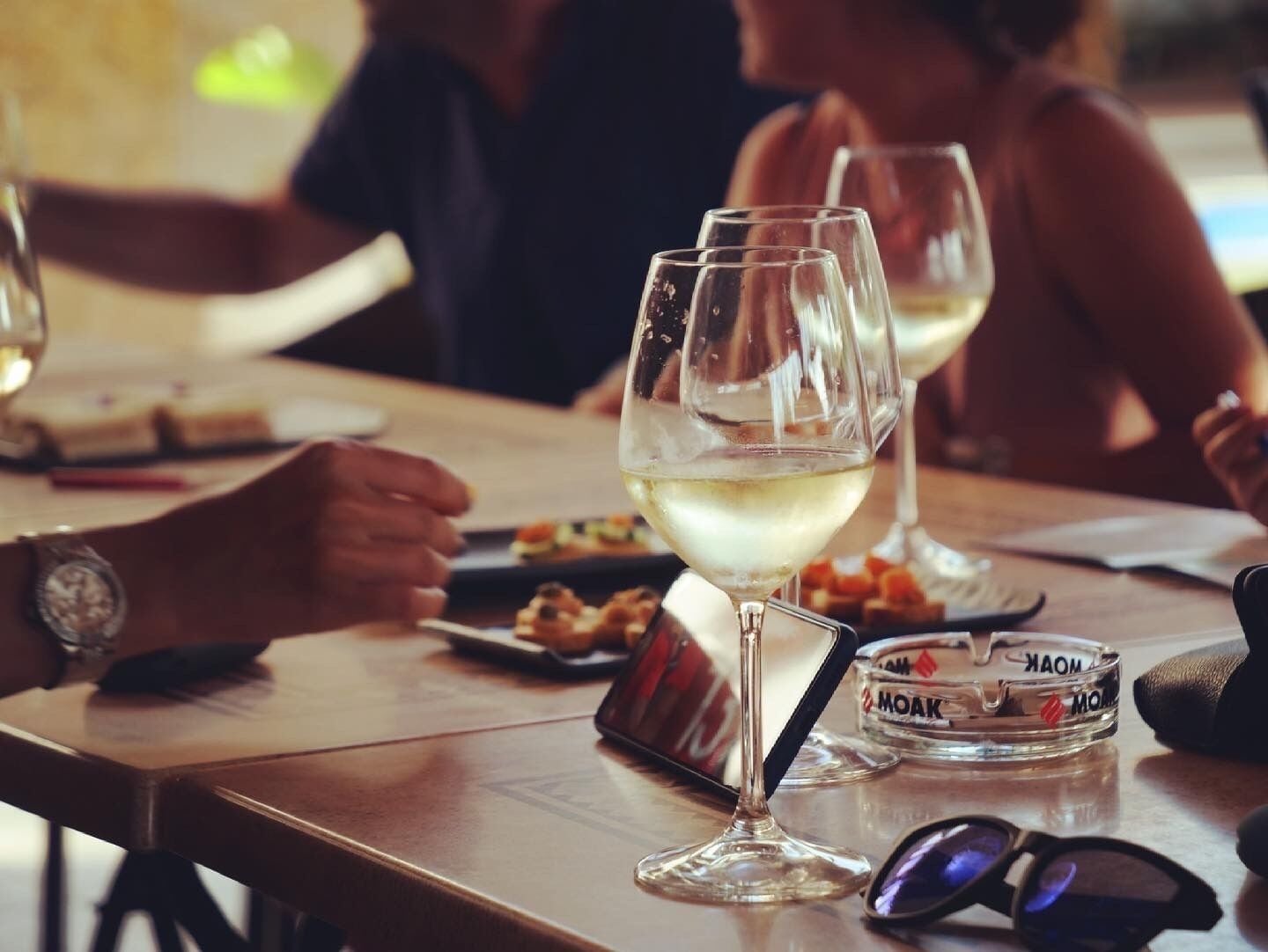 Una mesa de comedor con copas de vino, un teléfono inteligente y un paquete de cigarrillos.