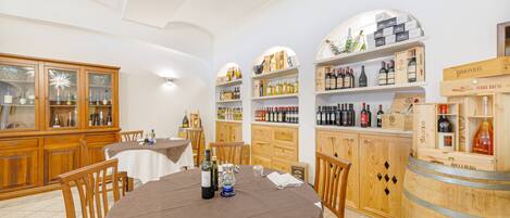 A dining area with wooden cabinets, a round table with a brown tablecloth, and wine bottles on shelves.