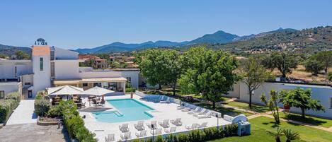 A hotel with a swimming pool, lounge chairs, and a view of the surrounding landscape.