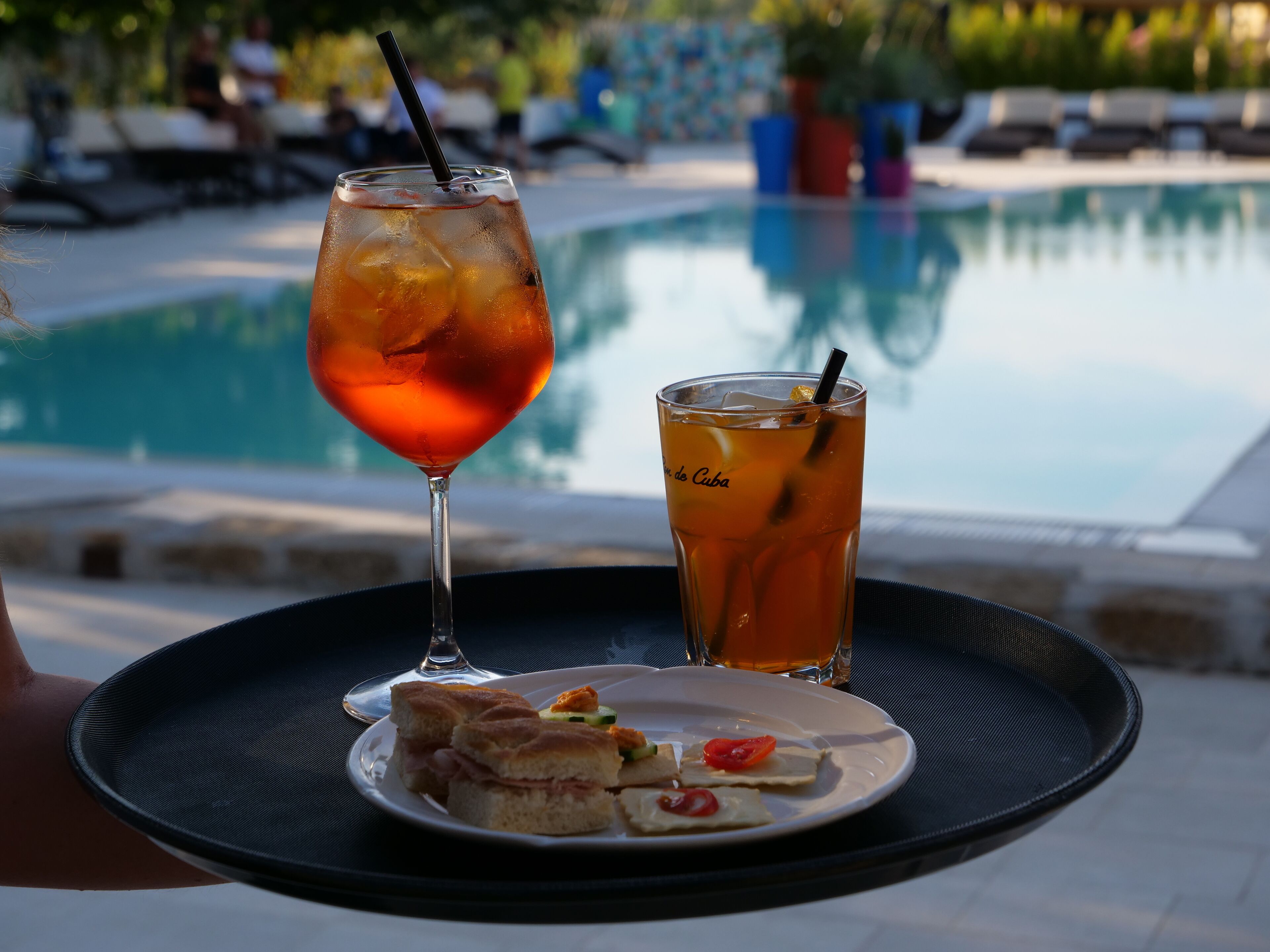 A tray with a glass of iced tea, a glass of water, and a plate of food near a pool.