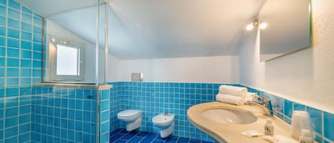 A bathroom with blue tiles, a sink, a mirror, and two toilets.