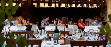 Un restaurante con mesas dispuestas para comer, con copas de vino y una botella.