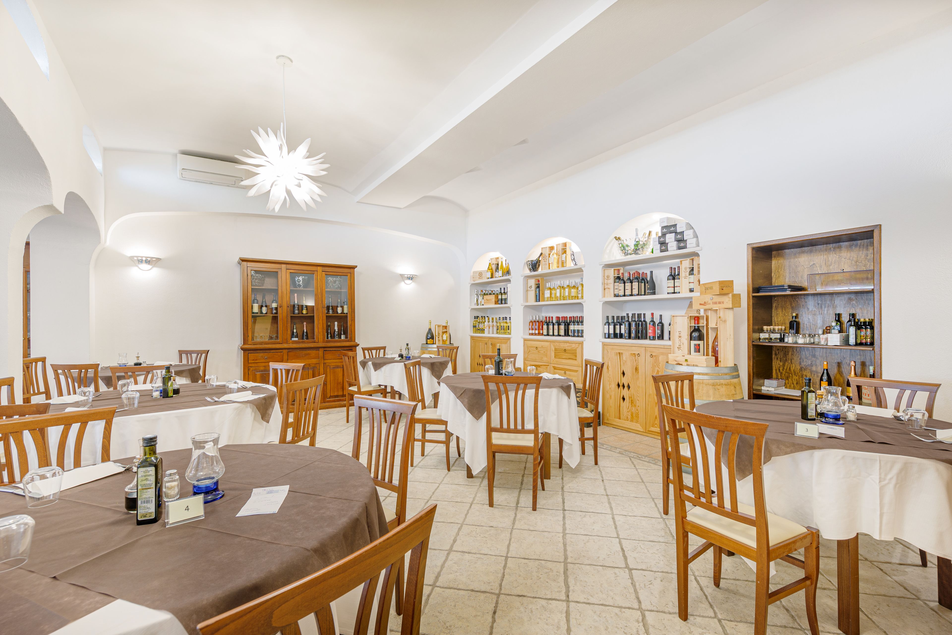 Un restaurante con varias mesas y sillas, una exhibición de vinos y un armario de madera.