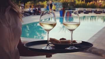 Une personne tenant un plateau avec deux verres de vin blanc et une assiette de nourriture, près d’une piscine.