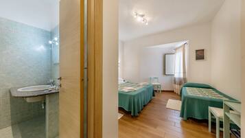 A bathroom with a sink and shower, a bedroom with a bed and desk, and a hallway.