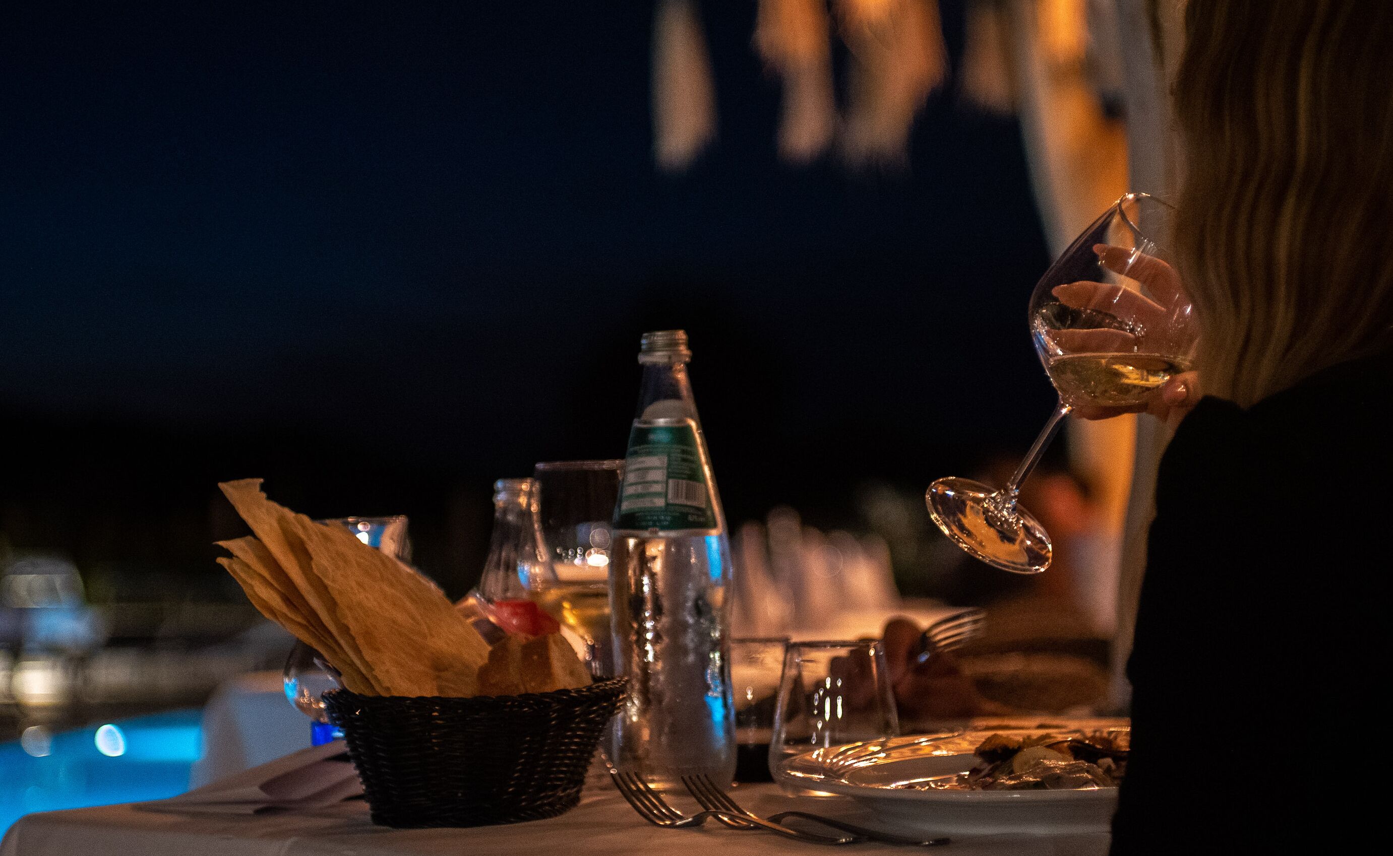 Una mesa con una botella, una copa y una cesta de pan.