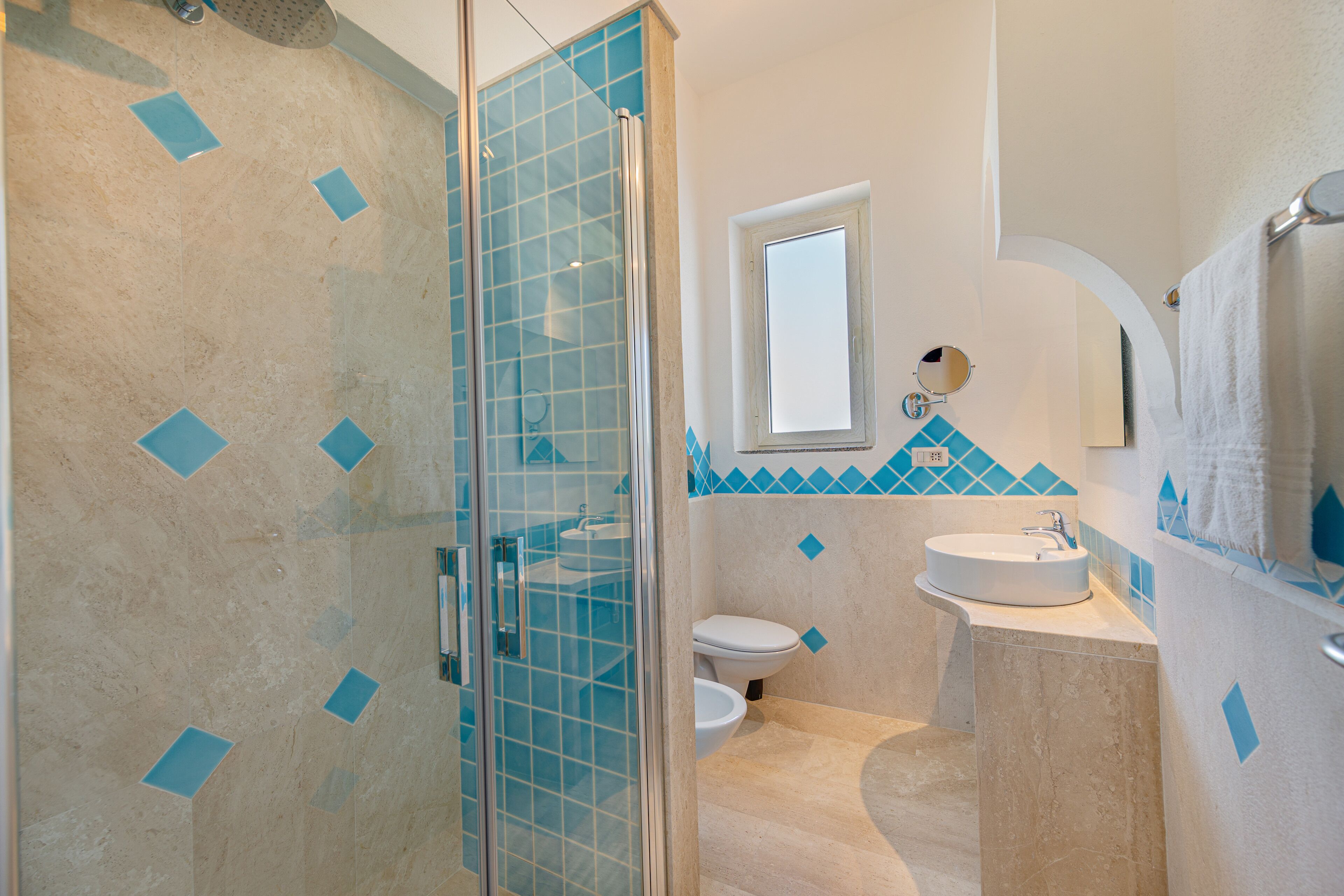 Un baño con cabina de ducha de vidrio, inodoro y lavamanos con espejo superior.