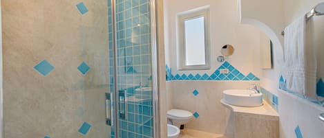 Un baño con cabina de ducha de vidrio, inodoro y lavamanos con espejo superior.