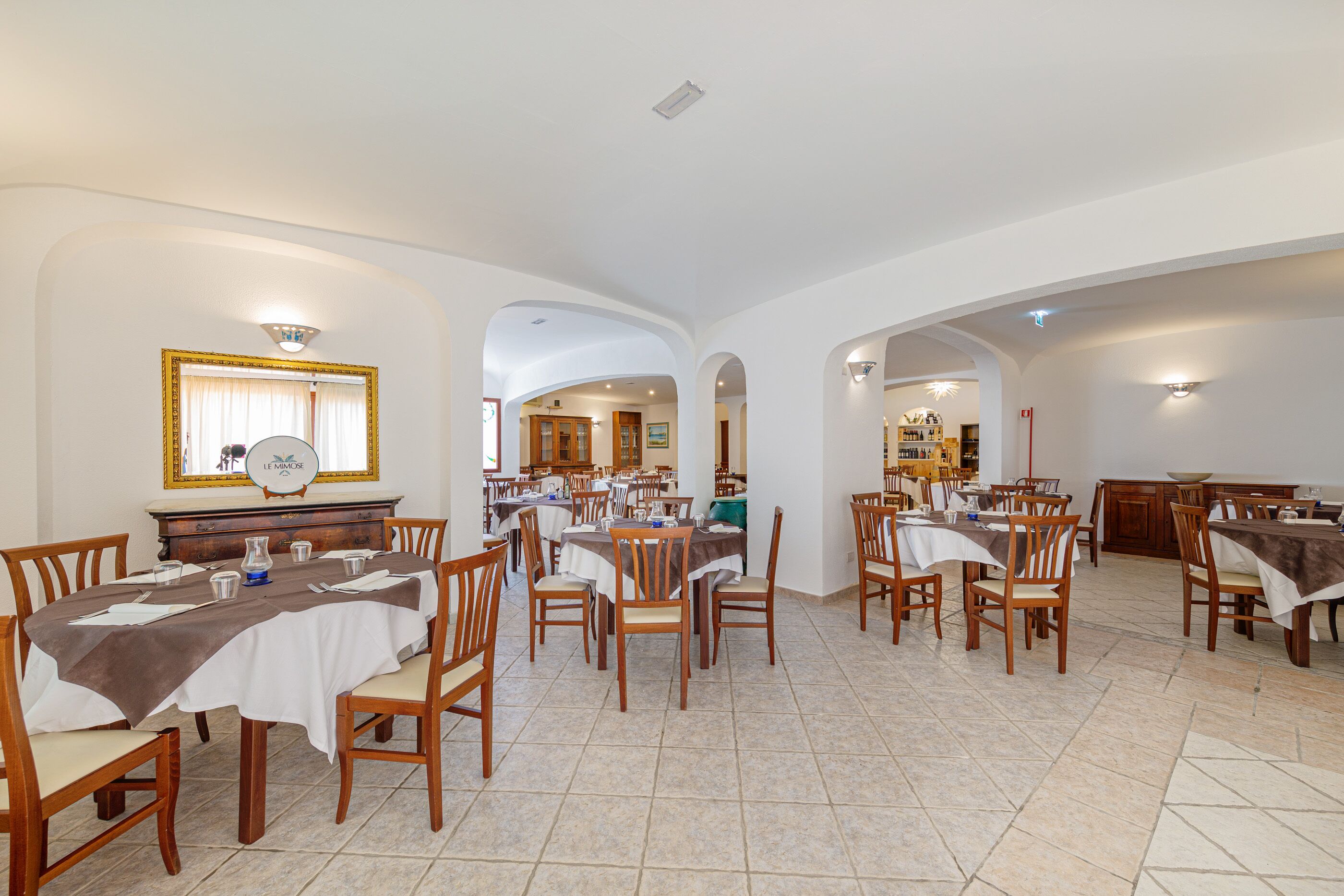 Un comedor espacioso con varias mesas y sillas, una chimenea en el centro y vista a otra habitación.