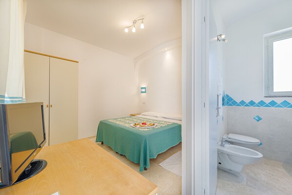 A bedroom with a bed, a desk, and a bathroom with a toilet and sink. - Hotel Le Mimose (San Teodoro)