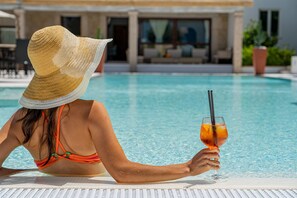A person relaxing by a pool with a drink, wearing a straw hat and an orange swimsuit.