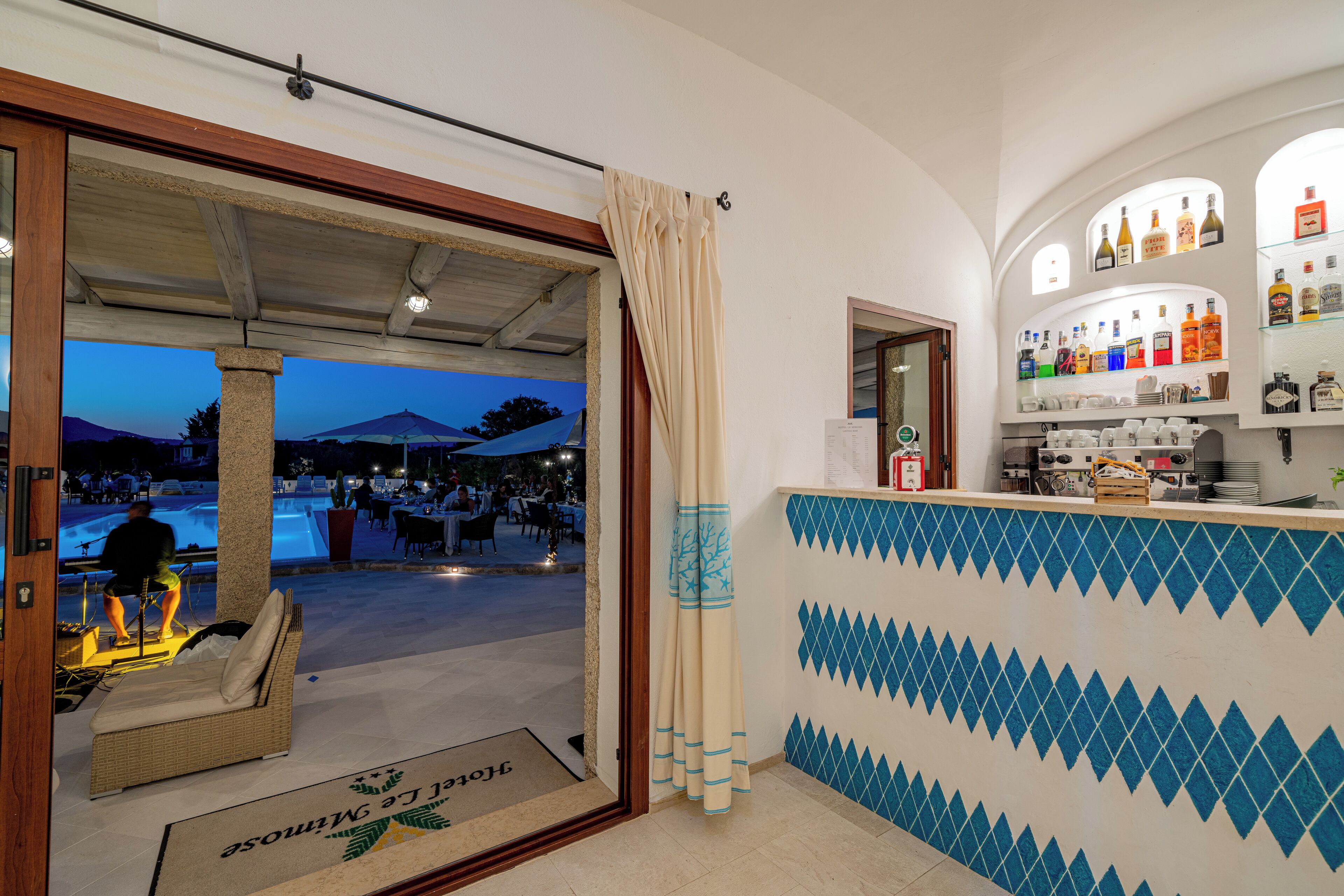 A bar area with a tiled wall and a view of an outdoor swimming pool at dusk.