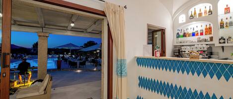 A bar area with a tiled wall and a view of an outdoor swimming pool at dusk.