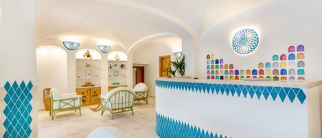 A hotel lobby with a reception desk, seating area, and a decorative wall with a geometric pattern.
