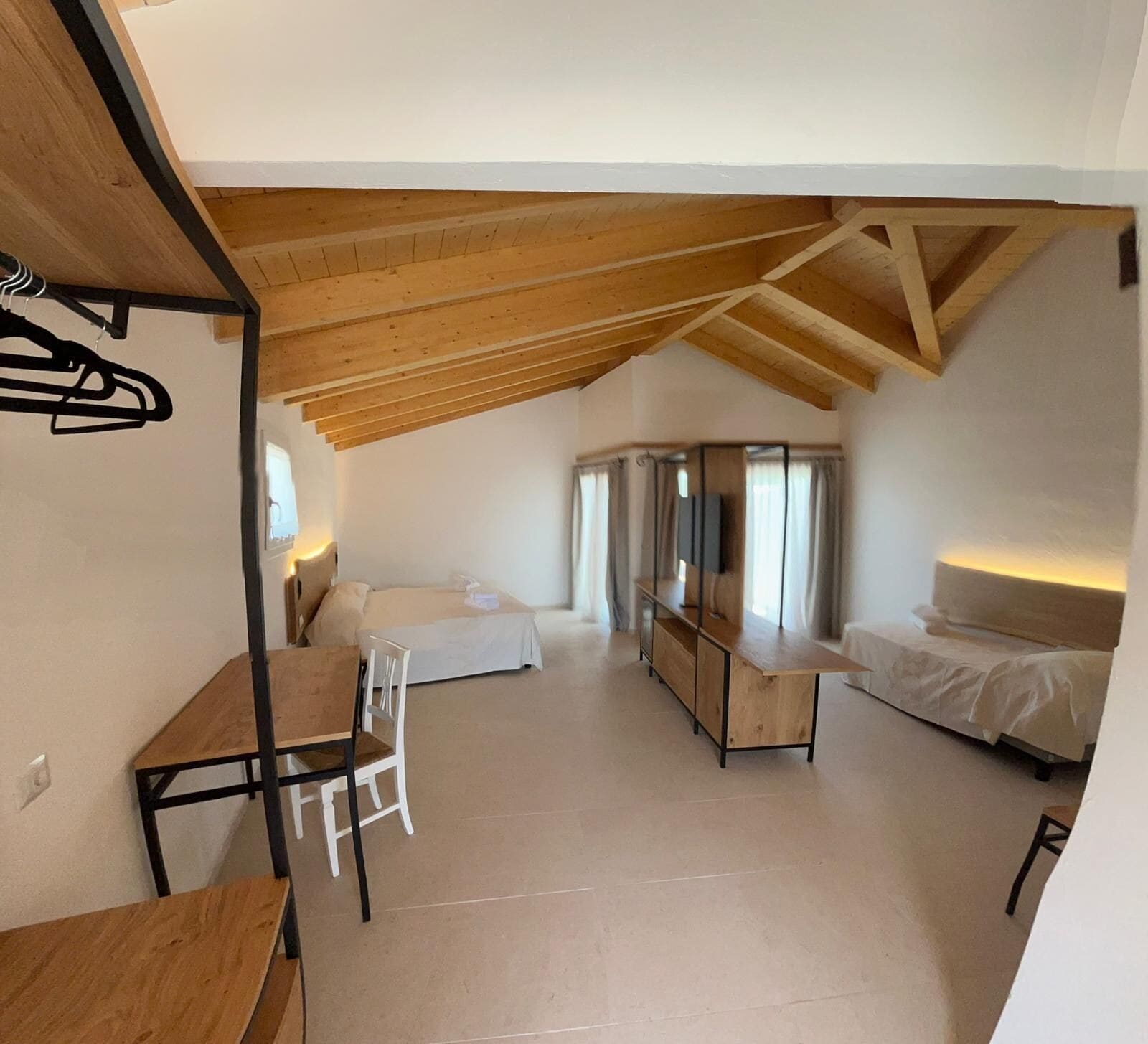 A compact, modern room with a sloped ceiling, a wooden desk, a white chair, a bed, and a small table.