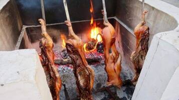 A large outdoor cooking area with a fire pit and several whole chickens being roasted.