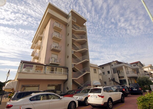 A multi-story residential building with balconies and a parking area with several cars. - Hotel Margherita (Jesolo)