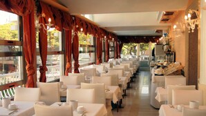 A restaurant with rows of white tables and chairs, red curtains, and chandeliers.