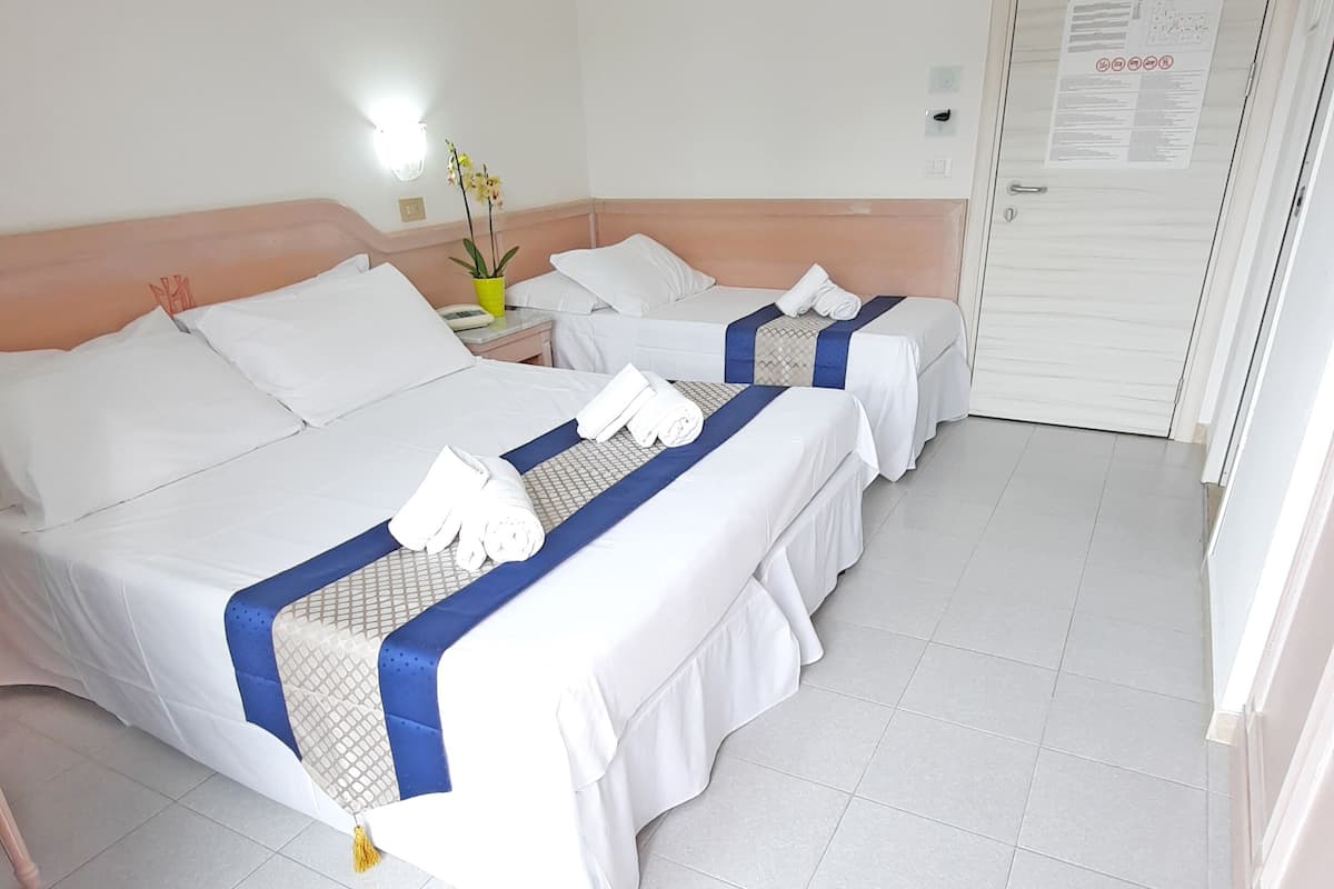 Une chambre d’hôtel avec deux lits, une table de chevet avec une lampe, une plante en pot et une porte avec une pancarte.