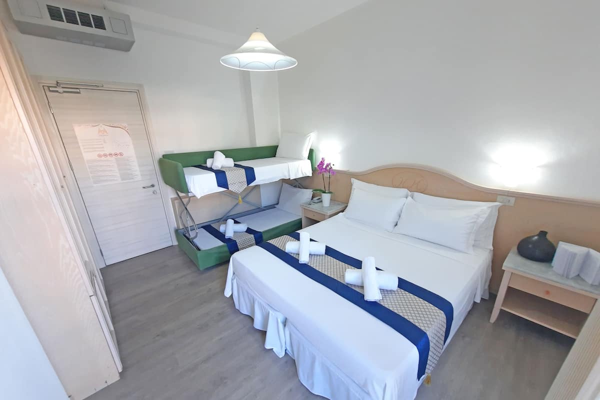 Une chambre d’hôtel avec un lit superposé, un lit simple, une table de chevet avec une lampe et une petite table de nuit.