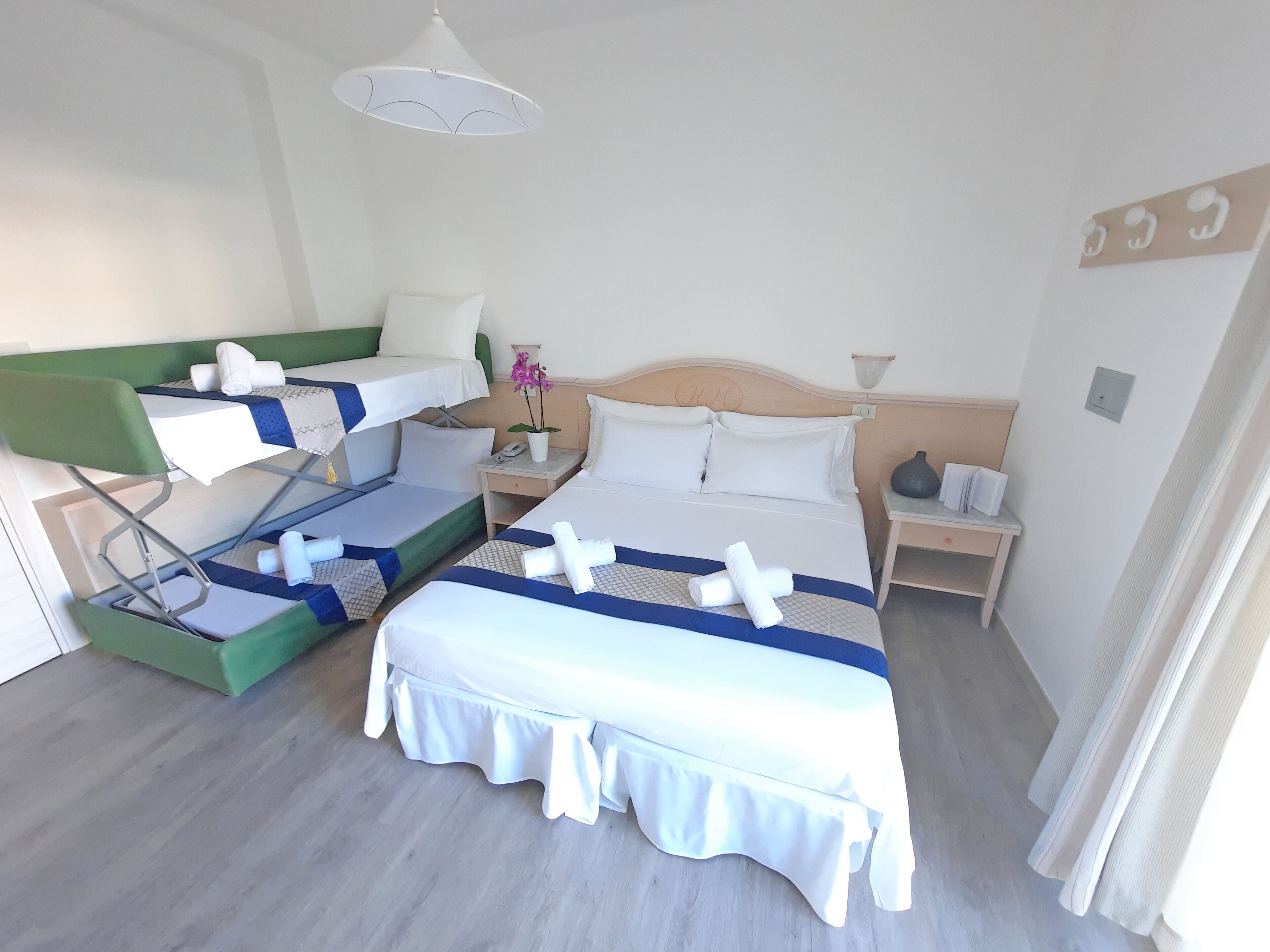 A hotel room with two beds, a small table with a phone, a nightstand, and a hanging light fixture.