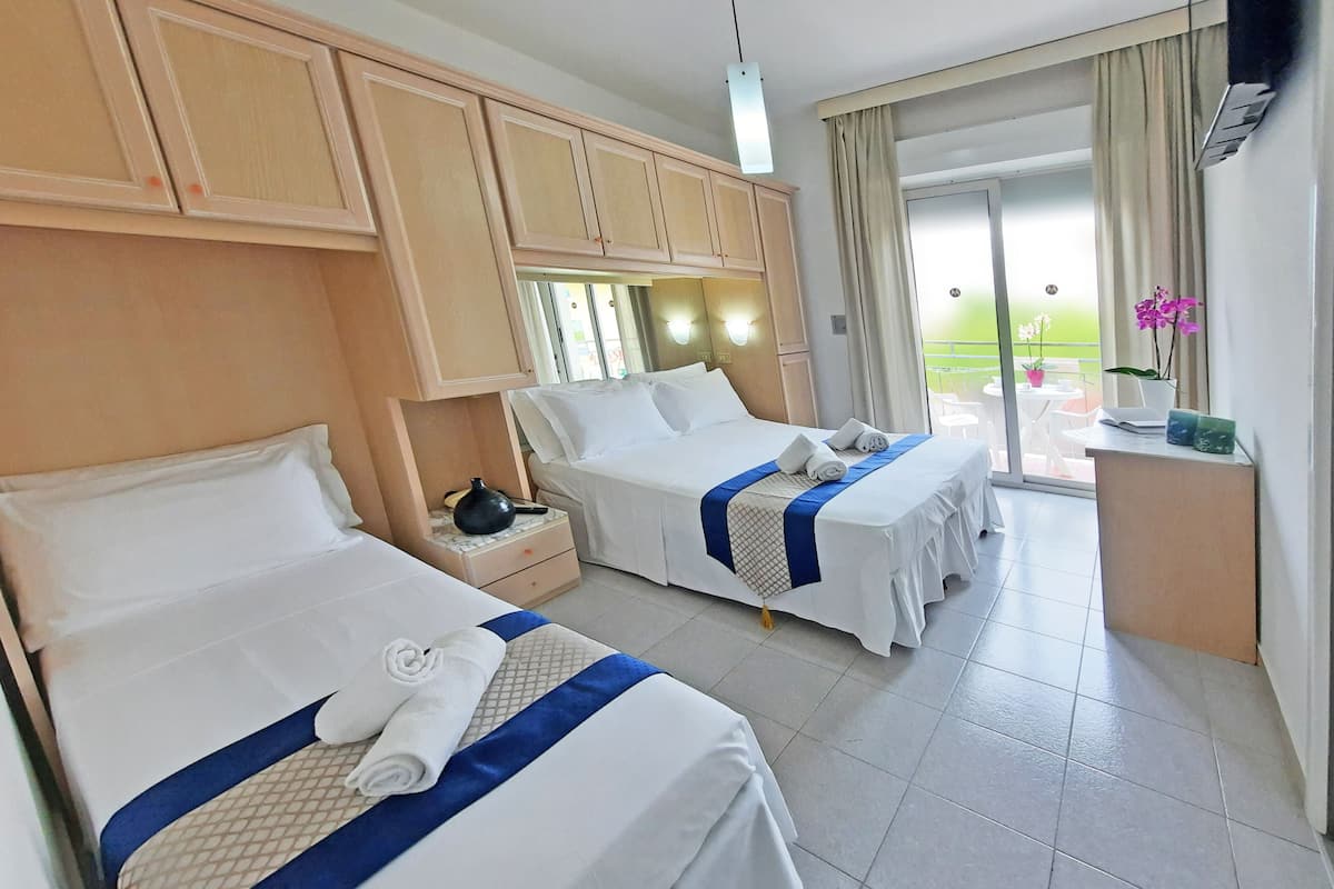 Une chambre d’hôtel avec deux lits, une petite table, une table de chevet, une fenêtre avec des rideaux et une vue sur l’extérieur.
