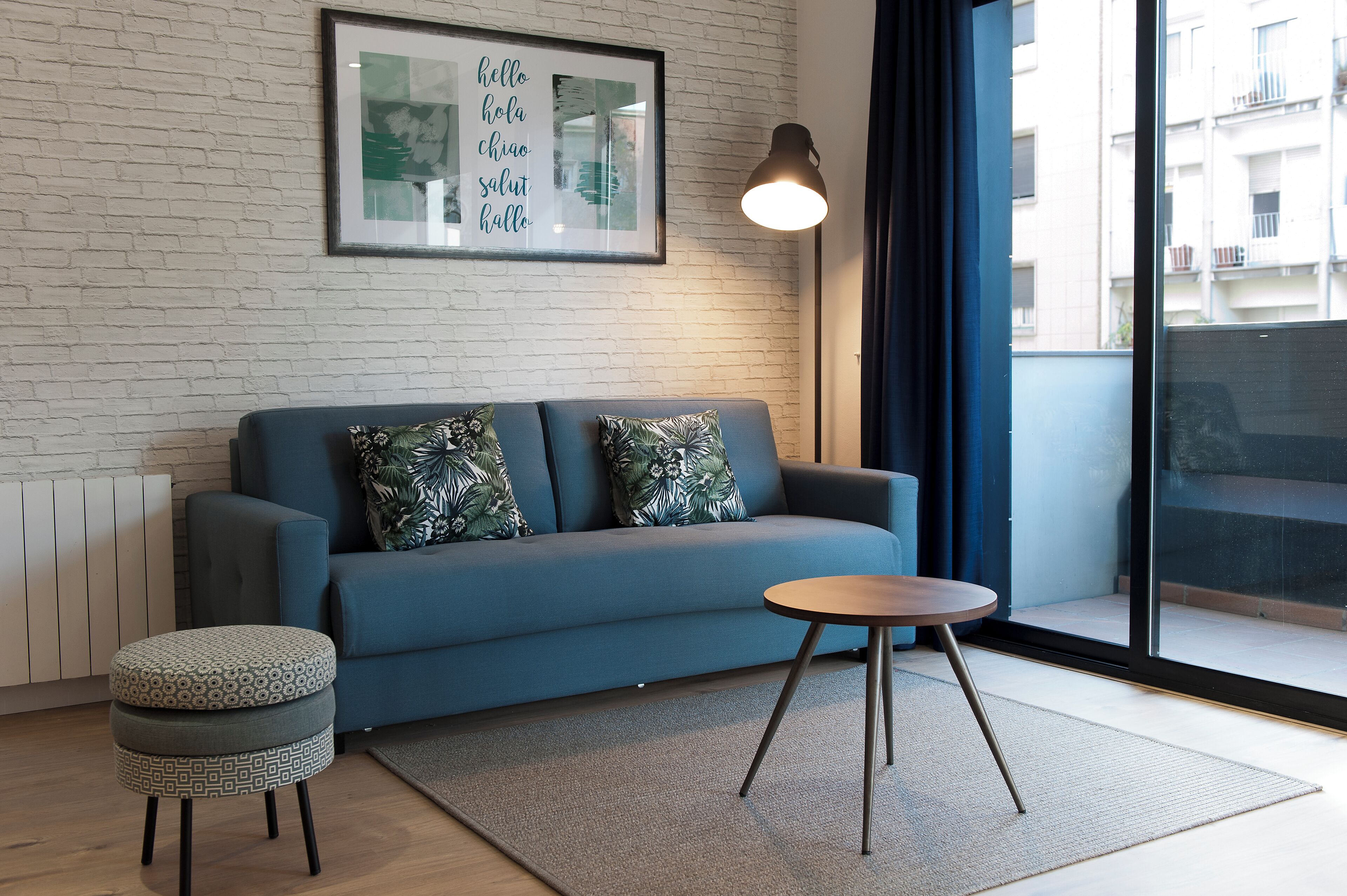 A modern living room with a blue sofa, patterned cushions, a round wooden table, and a framed multilingual sign on the wall.
