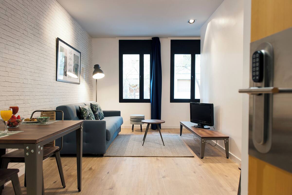 A modern living room with a sofa, a dining table, a TV, and a refrigerator.
