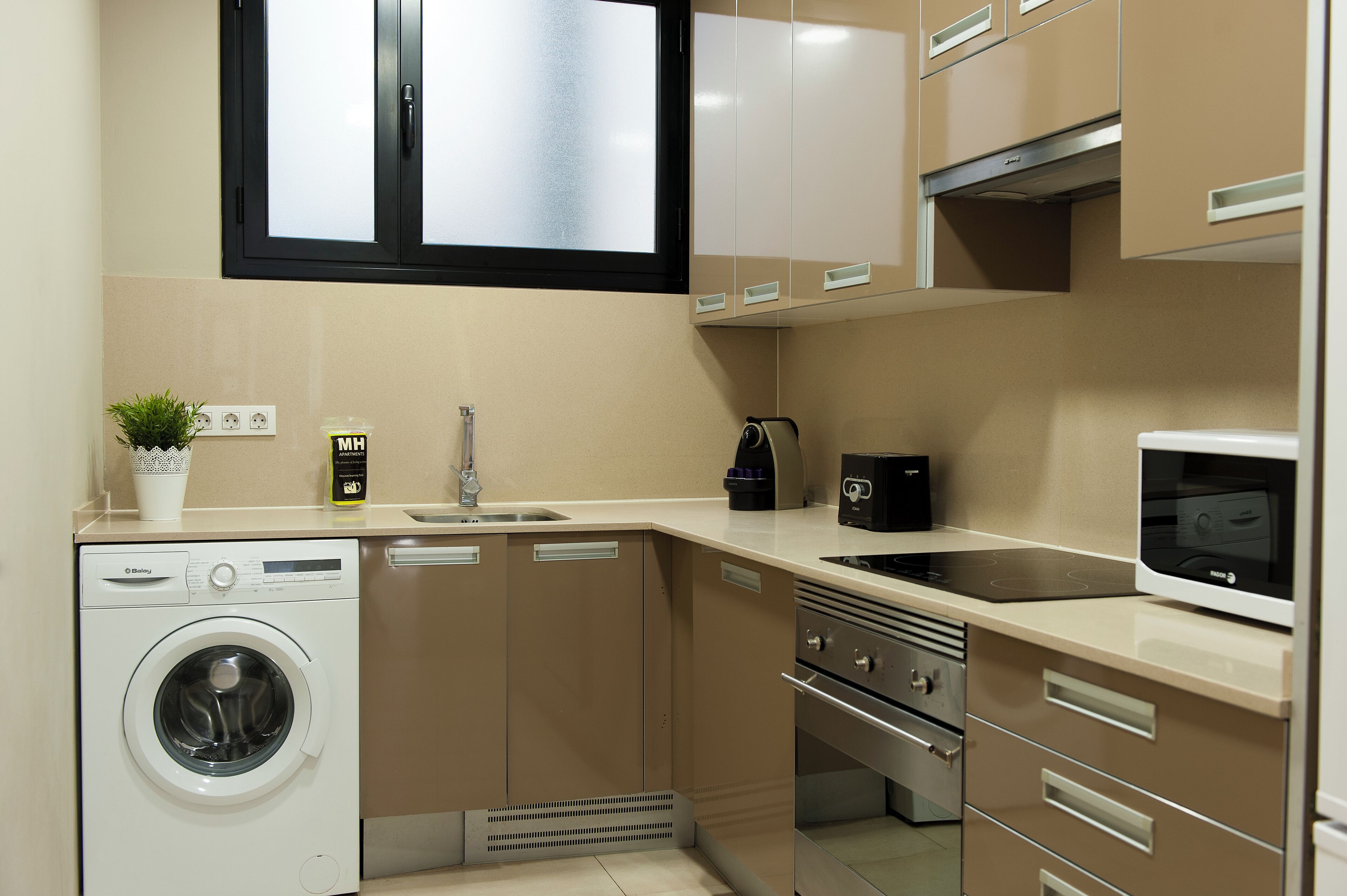 A compact kitchen with a washing machine, a microwave, a stove, and a sink.