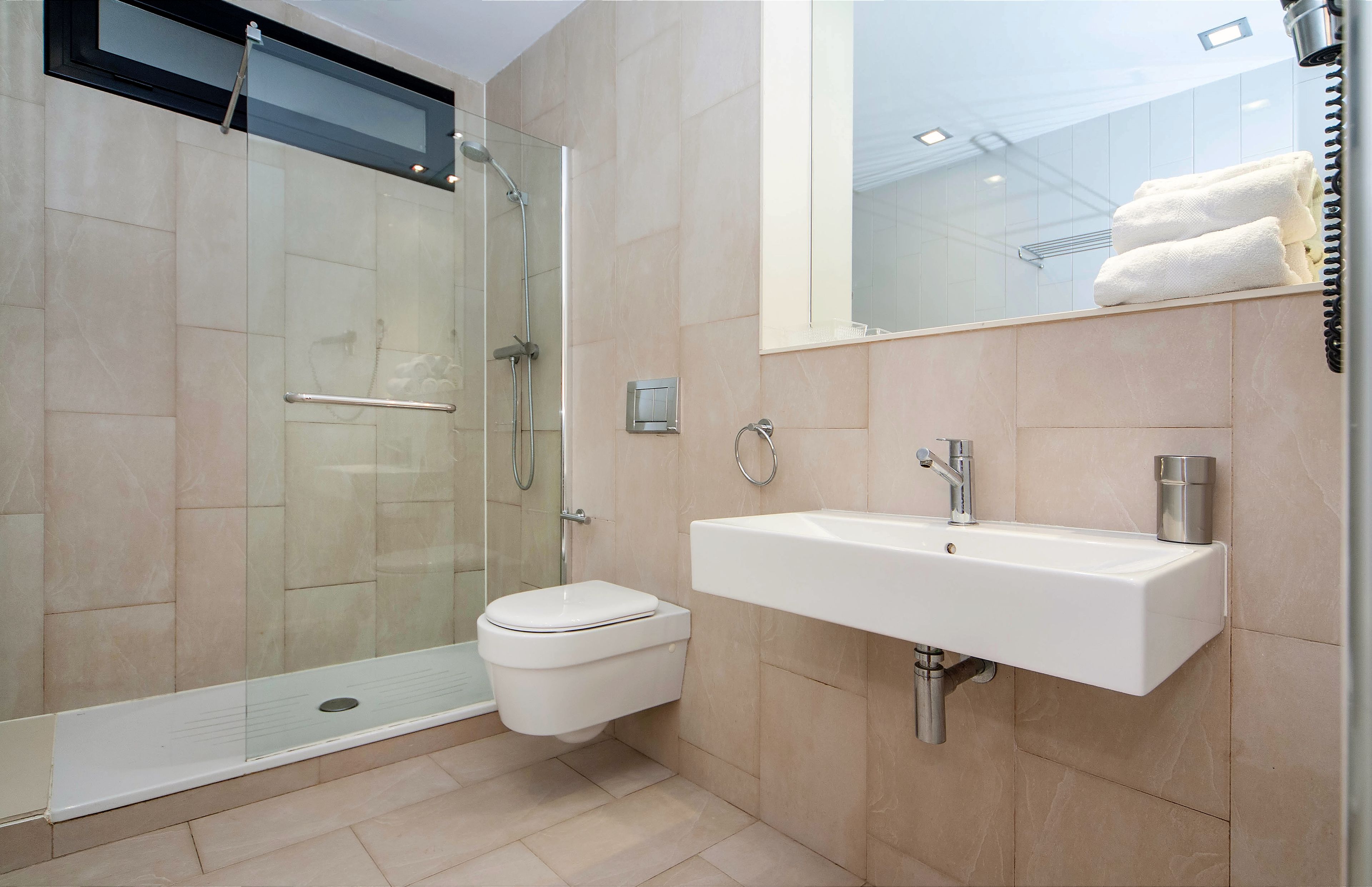 Un baño moderno con ducha de vidrio, inodoro blanco y lavamanos empotrado.