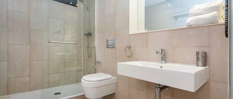 Un baño moderno con ducha de vidrio, inodoro blanco y lavamanos empotrado.