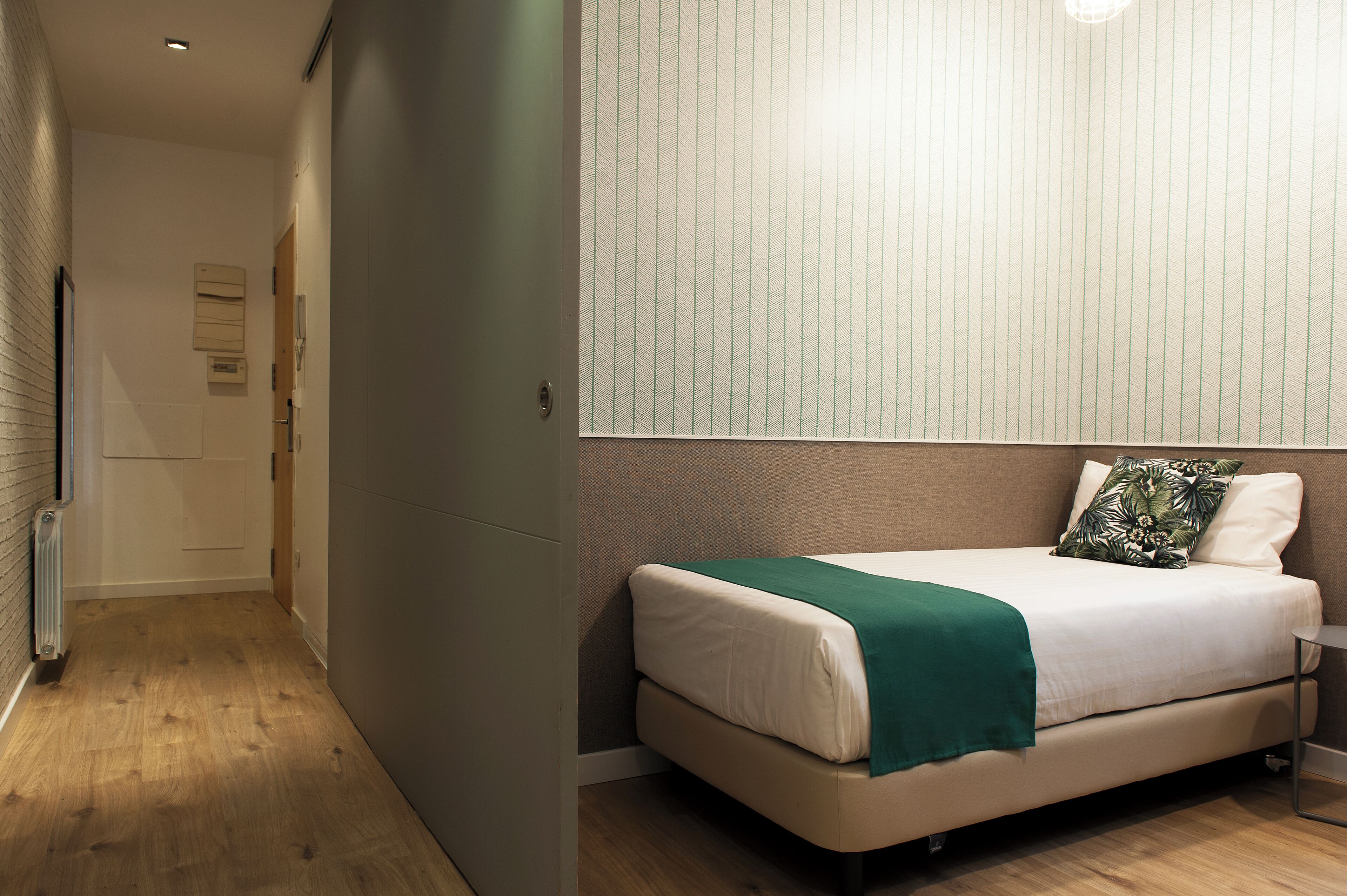 Een slaapkamer met een bed, een groene plaid en een kussen met een bladmotief.