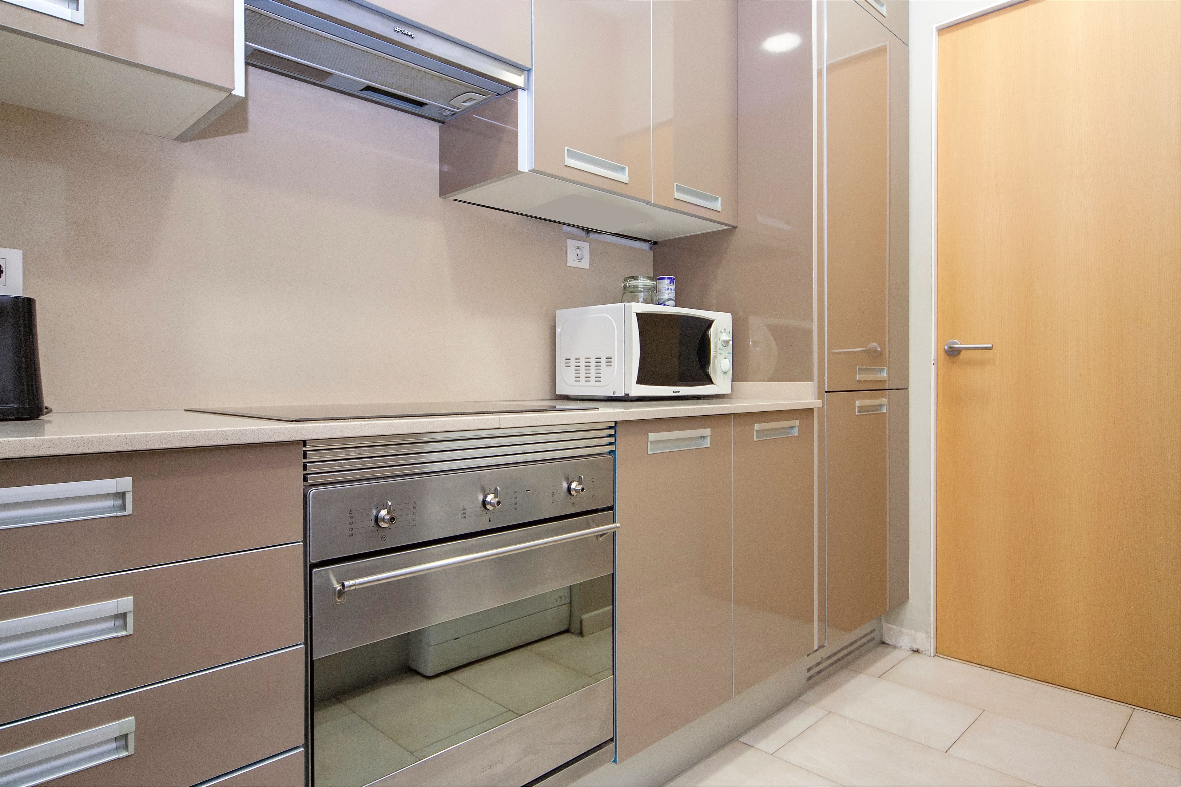 A kitchen with stainless steel appliances, a microwave, and a wooden door.