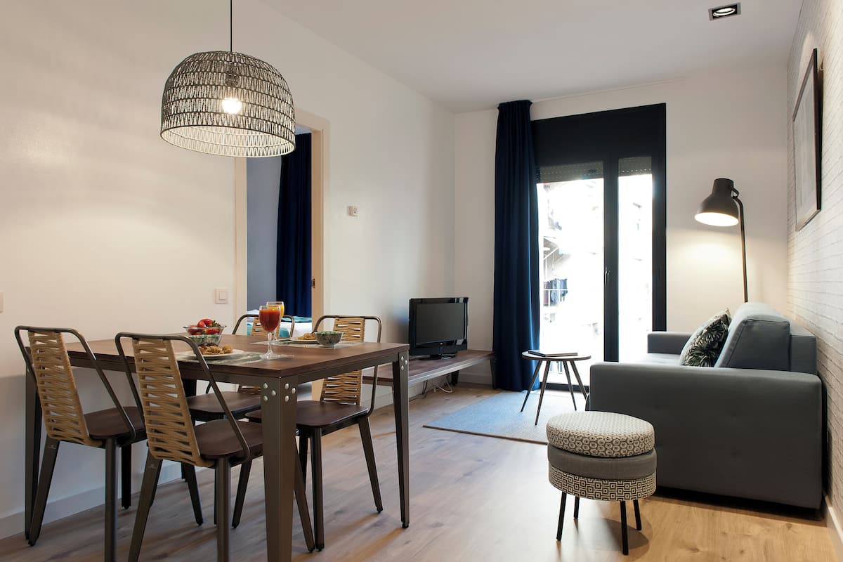 A modern living room with a dining area, a grey sofa, a TV, and a hanging light fixture.