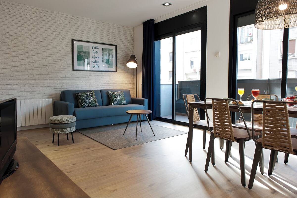 A modern living room with a blue sofa, a small round table, and a dining area with wooden chairs.