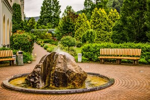 A garden with a central rock fountain, benches, and a paved walkway. - Hotel Zdravilisce Lasko (Lasko)