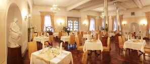 A dining area with multiple tables set for service, each with a white tablecloth and gold accents. - Hotel Zdravilisce Lasko (Lasko)