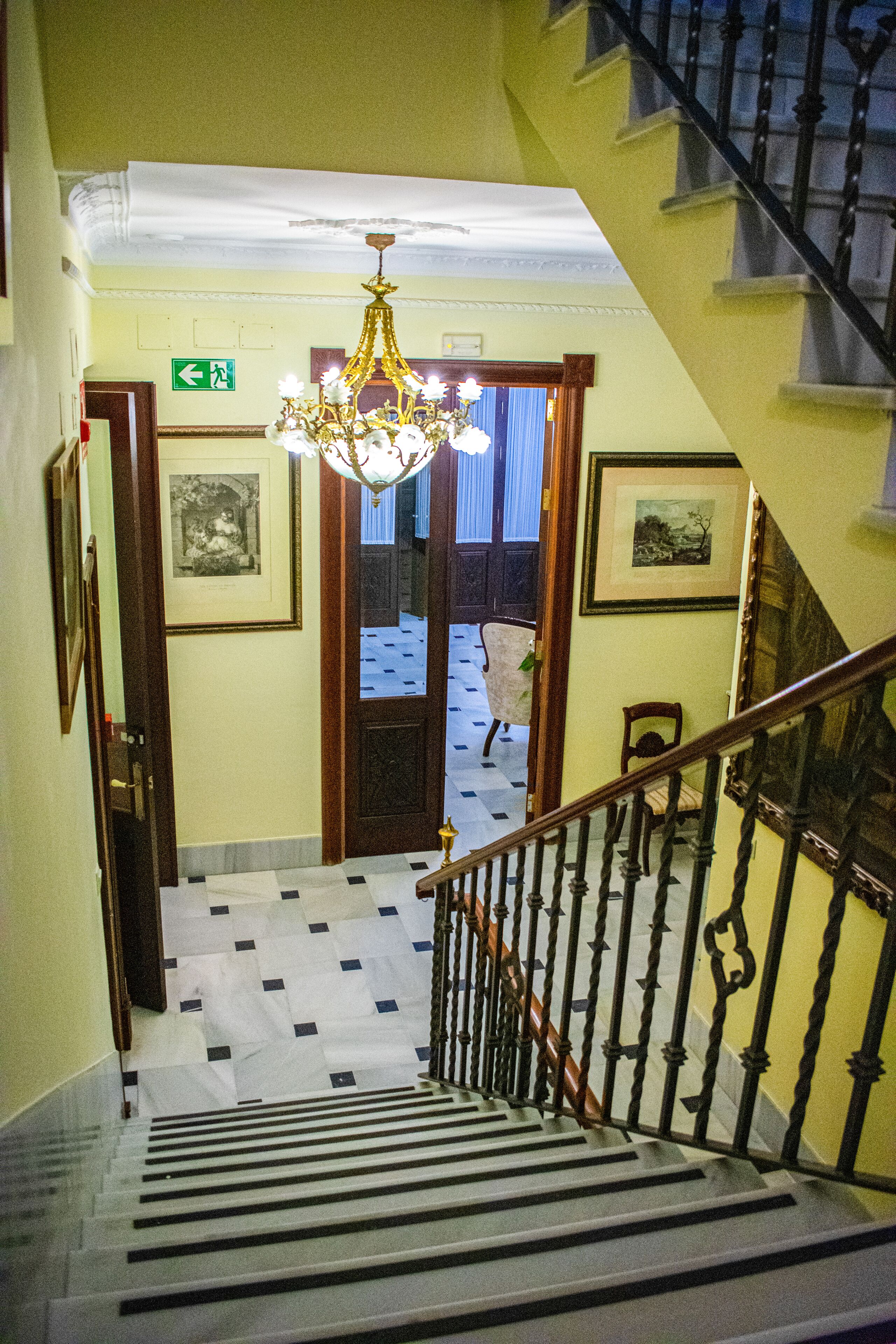 Eine Treppe mit einer Chandelüster, eine Tür mit einem Ausgangsschild und ein strukturierter Boden.