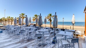 Un área al aire libre con mesas y sillas, una terraza de madera y vistas a la playa y al océano.